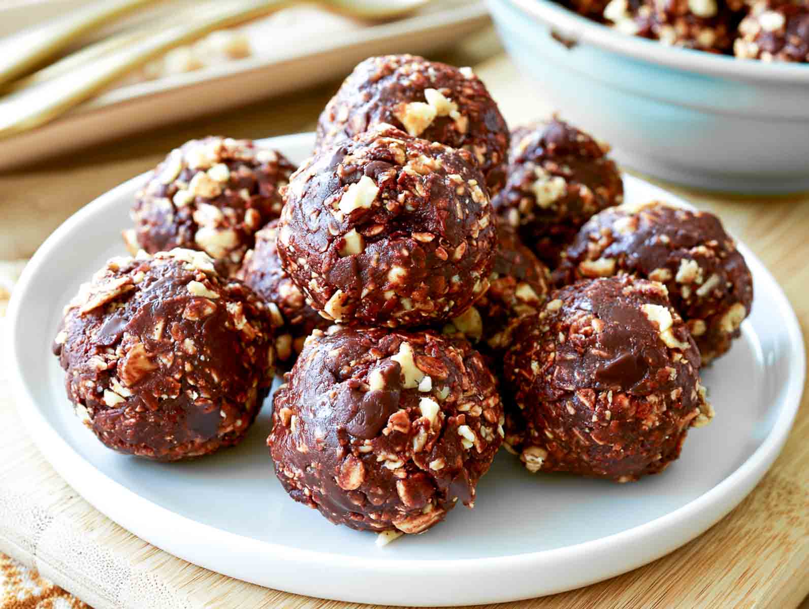 Chocolate oatmeal high-protein energy balls with rolled oats on a ceramic plate, with bowls of almonds and oats behind.