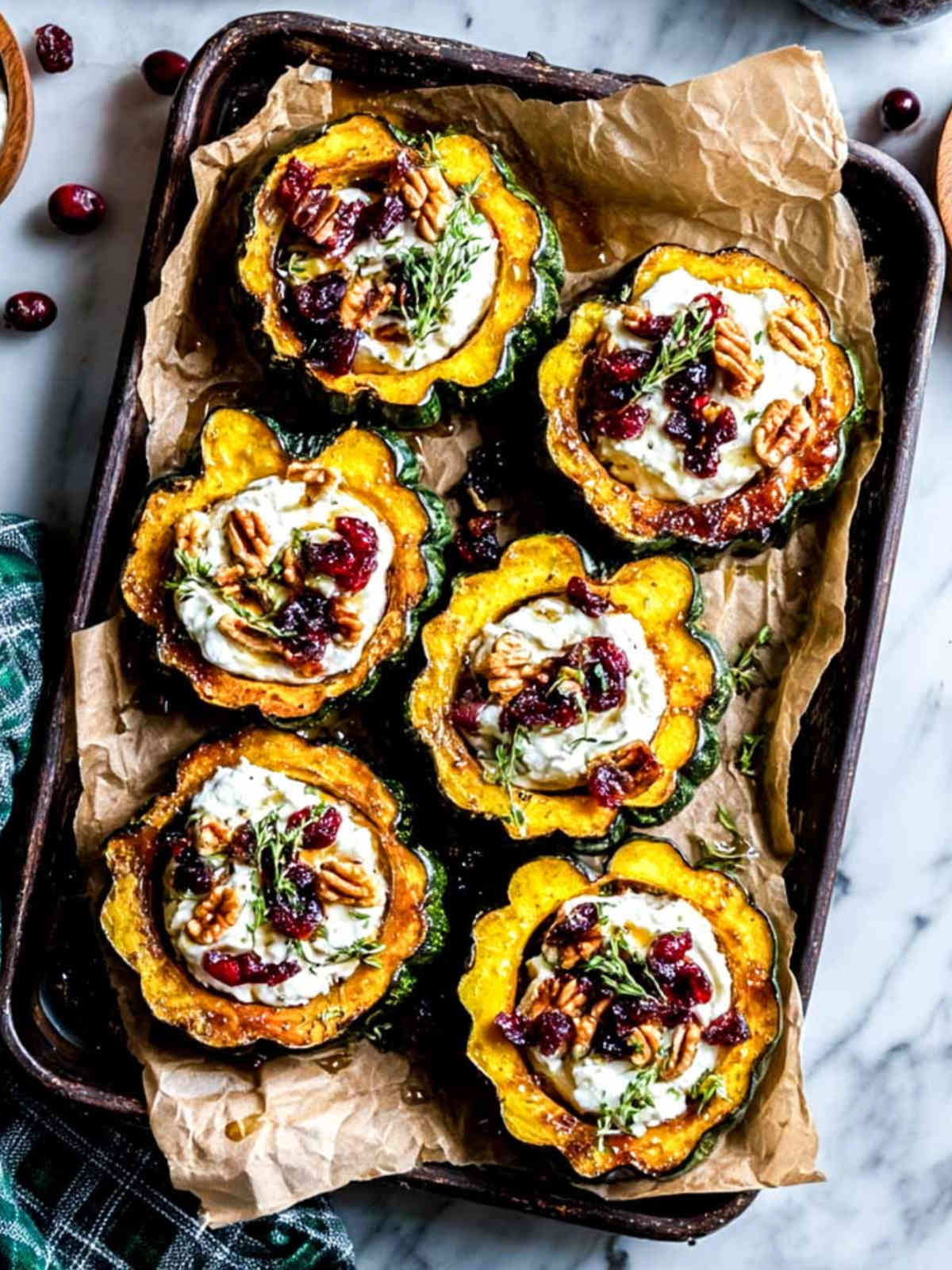 Six acorn squash boats on a parchment-lined baking tray, filled with whipped cottage cheese, cranberries, pecans, and thyme.
