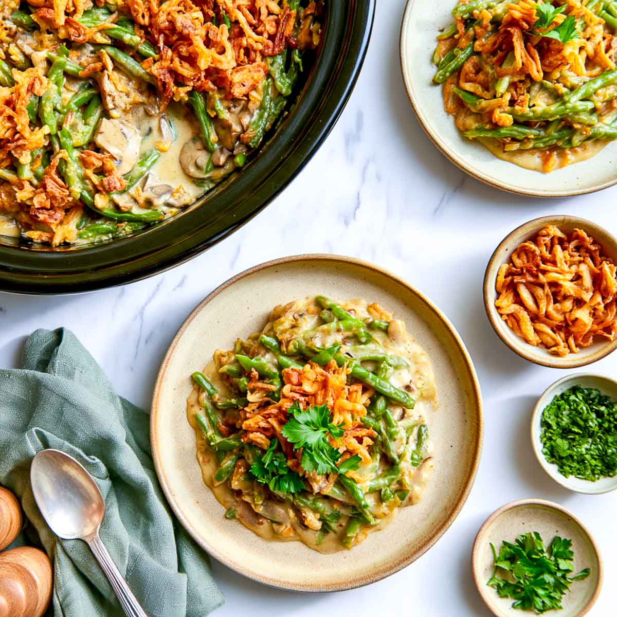 Crockpot green bean casserole on a stoneware plate topped with crispy fried onions and parsley, beside the slow cooker.