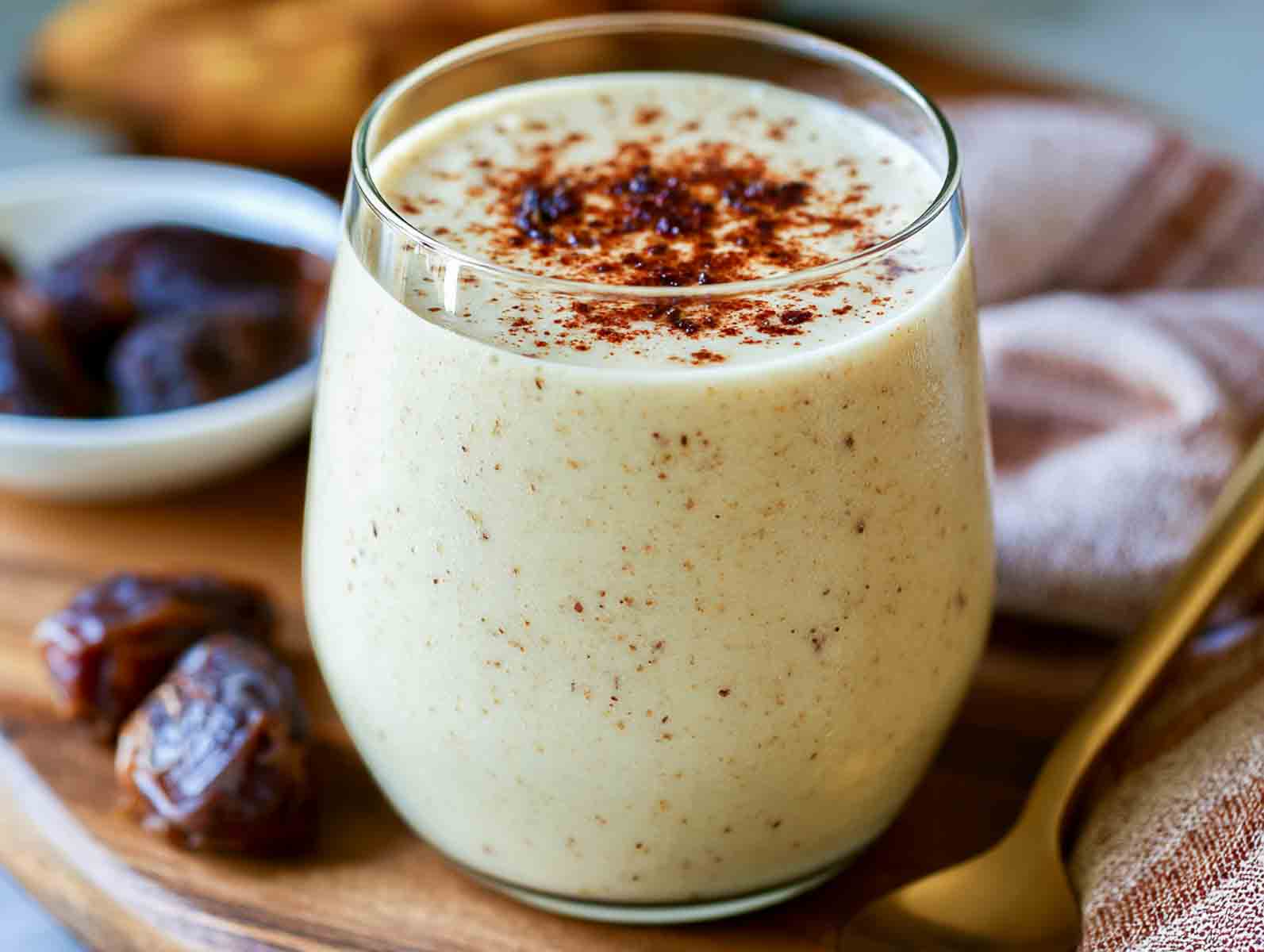 Creamy date kefir smoothie in a glass dusted with cinnamon, with Medjool dates alongside.