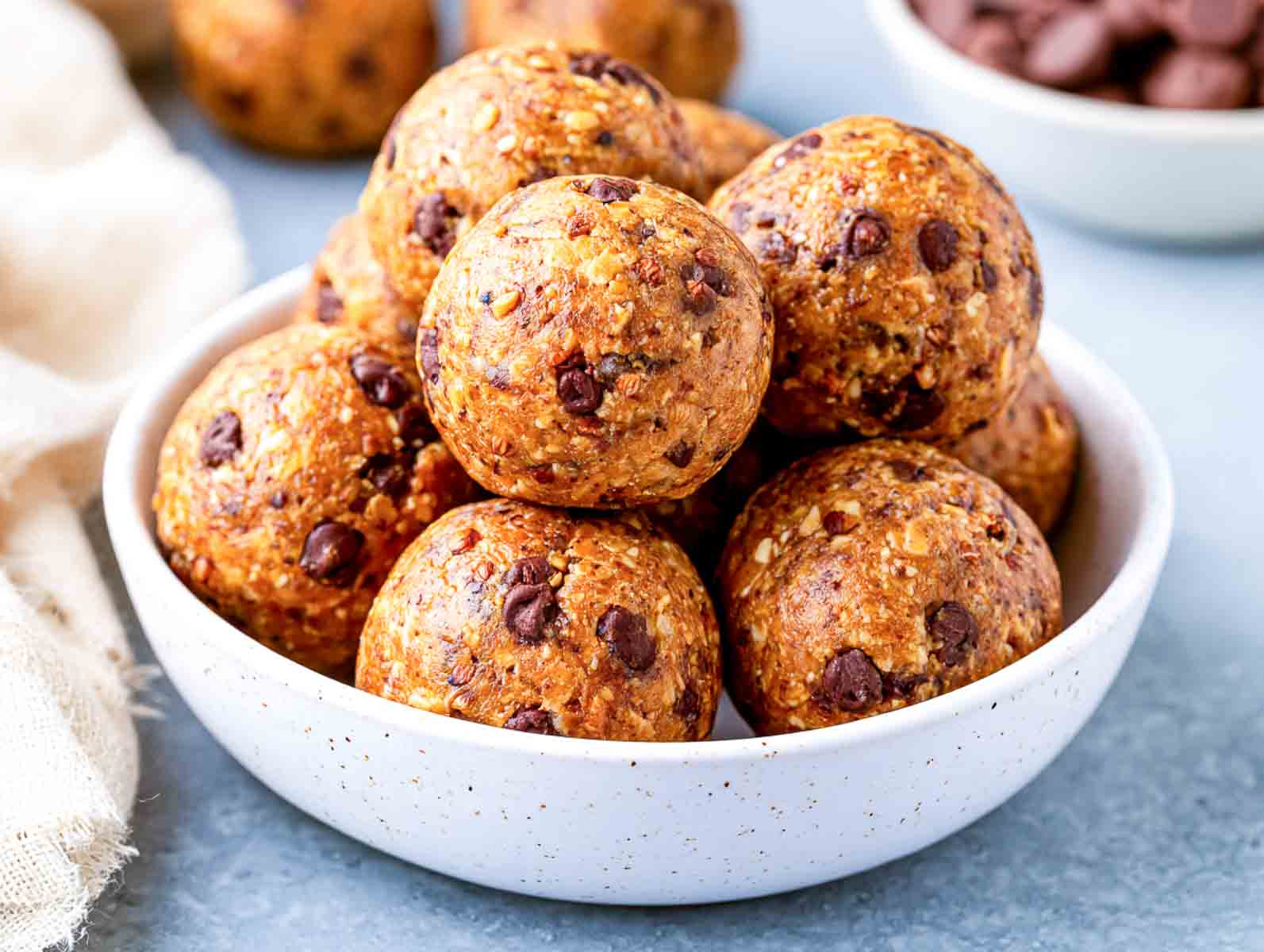 Gluten-free chocolate chip high-protein energy balls in a speckled white bowl, with a bowl of chocolate chips behind.