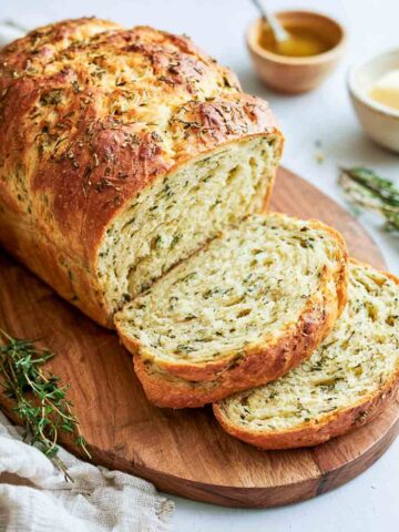 Sliced kefir bread with fresh herbs on a round wooden board with butter and honey.