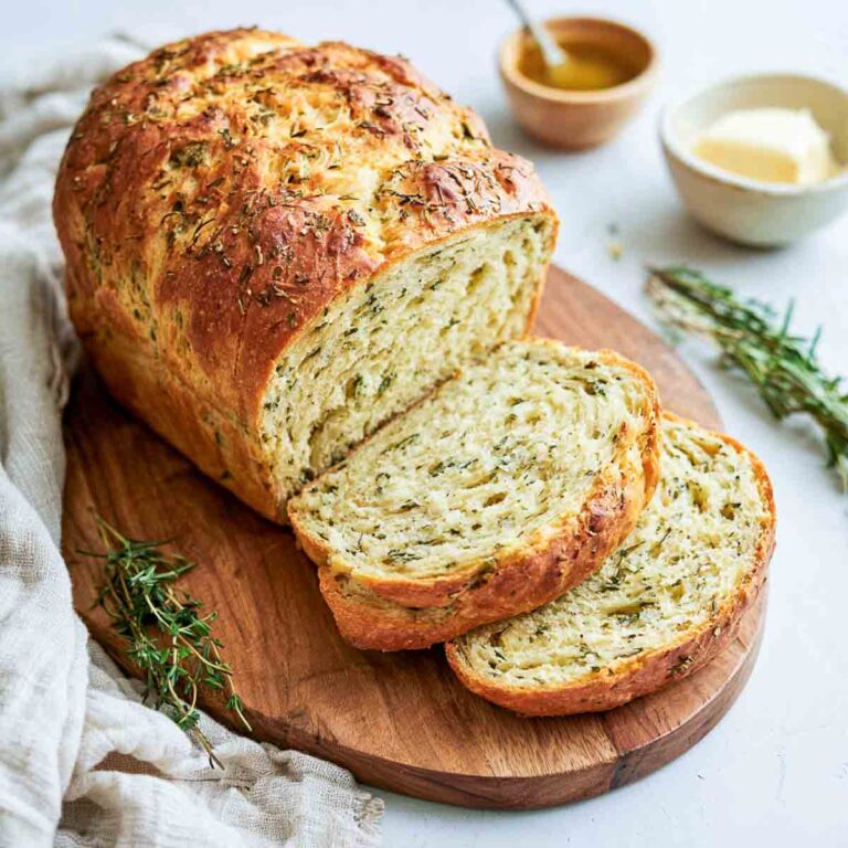 Sliced kefir bread with fresh herbs on a round wooden board with butter and honey.