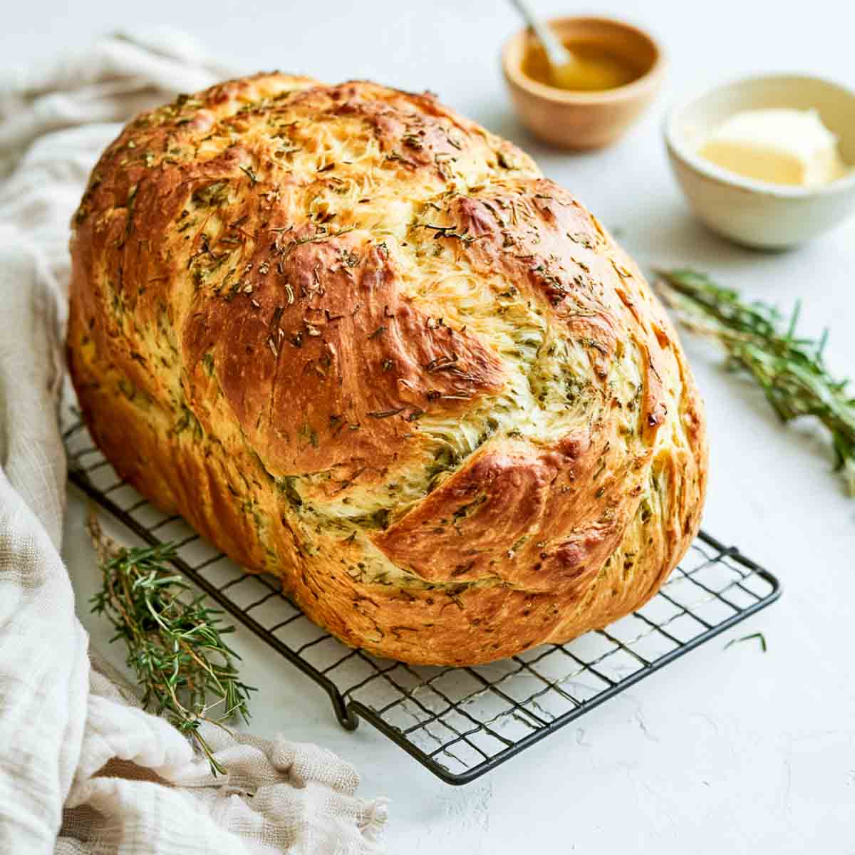 Whole baked kefir bread loaf cooling on a wire rack beside fresh rosemary and thyme.