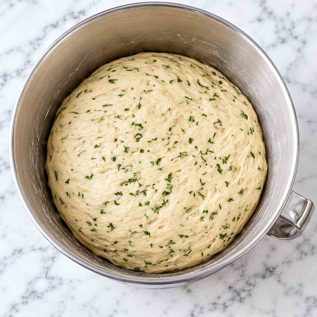 Risen kefir bread dough doubled in a stand mixer bowl, flecked with green herbs.