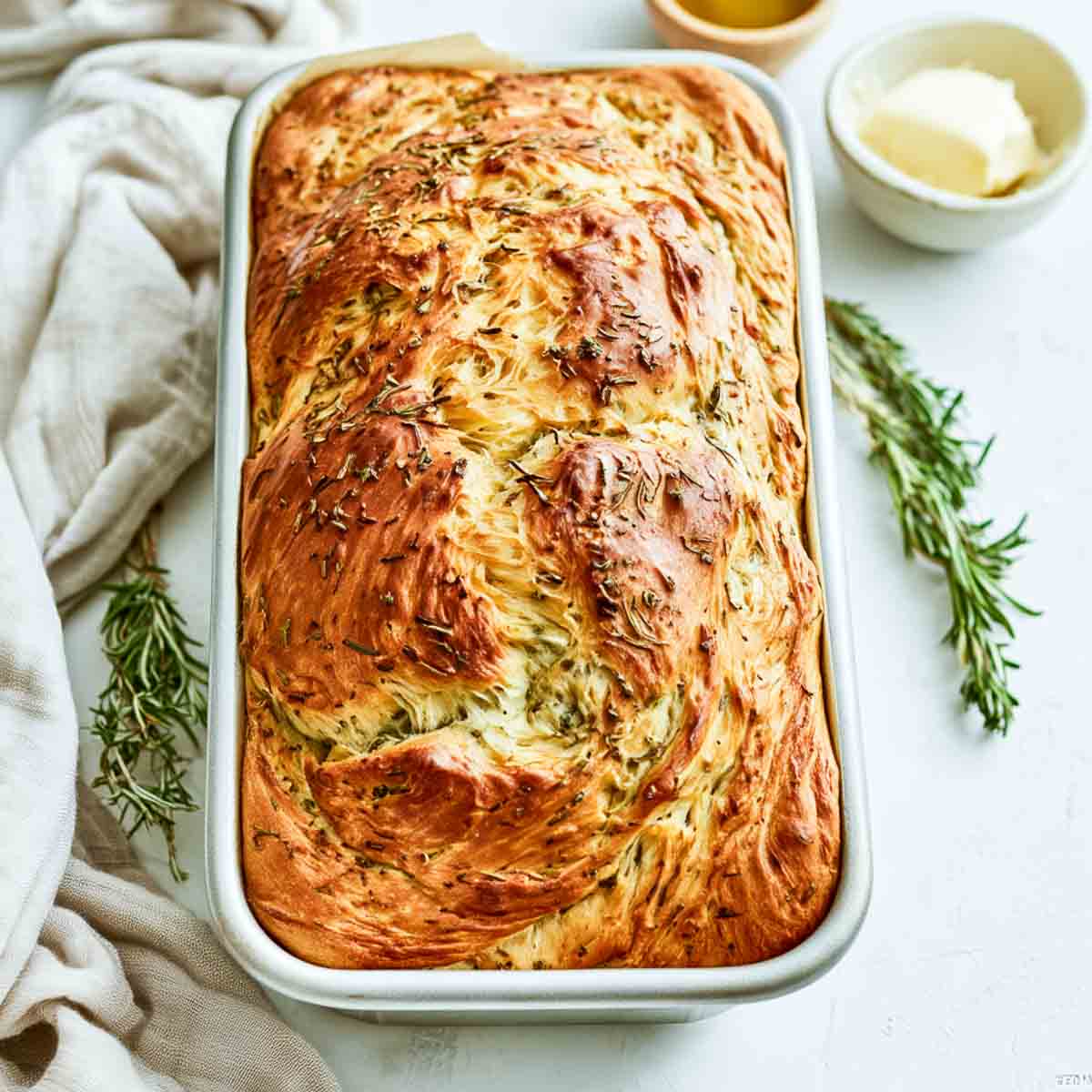 Baked kefir bread risen above the rim of the loaf pan with a golden herb-flecked crust.