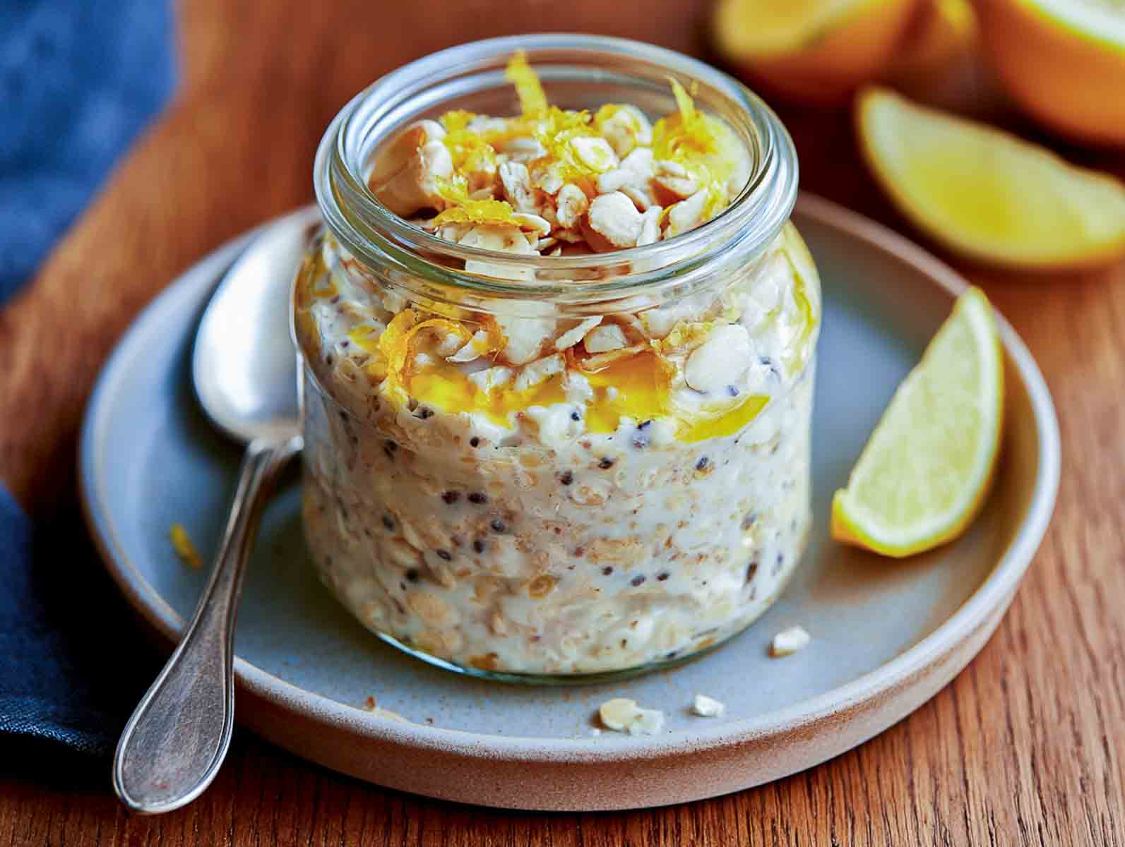Lemon kefir overnight oats in a glass jar topped with lemon zest, chopped cashews, and honey, with a lemon wedge.