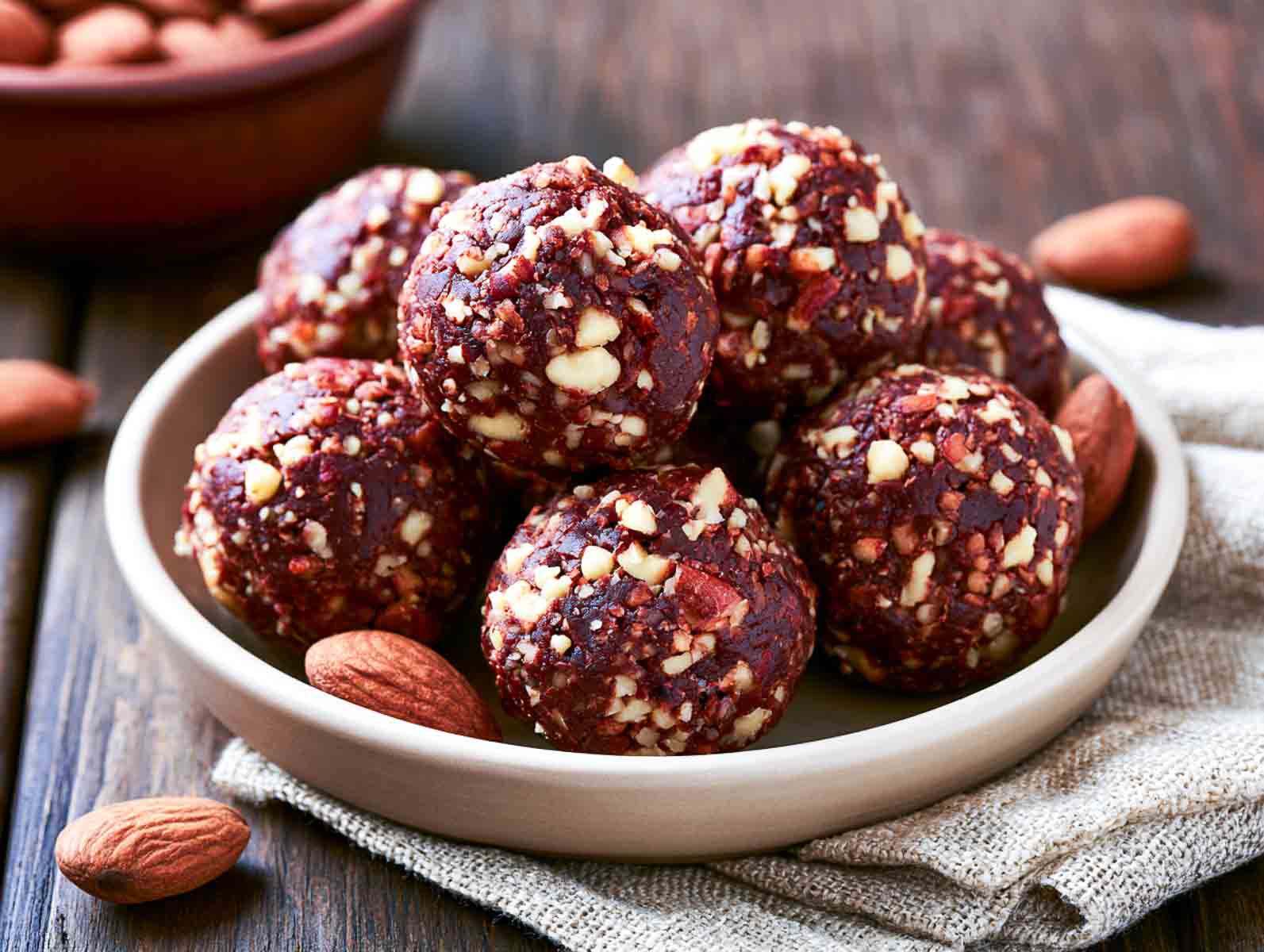 Low carb almond chocolate high-protein energy balls topped with chopped almonds and dark chocolate shavings, one bitten open, in a white bowl.