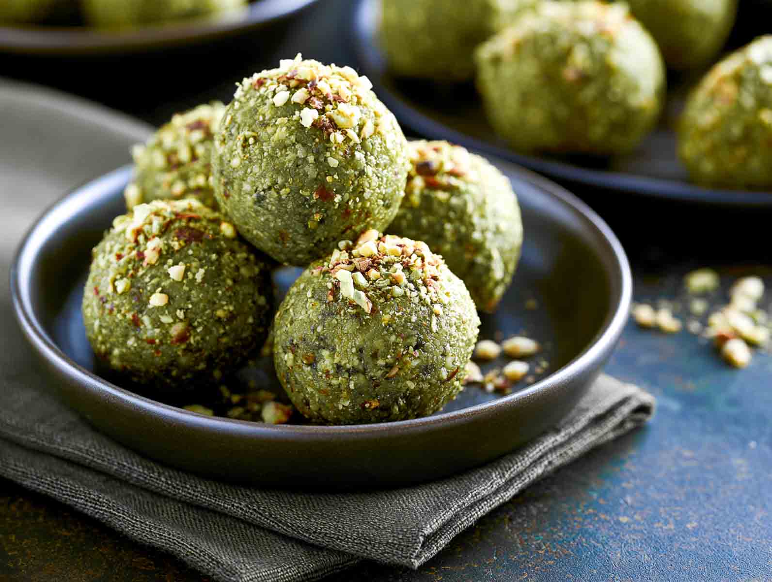 Low carb matcha almond high-protein energy balls topped with chopped almonds in a dark bowl.