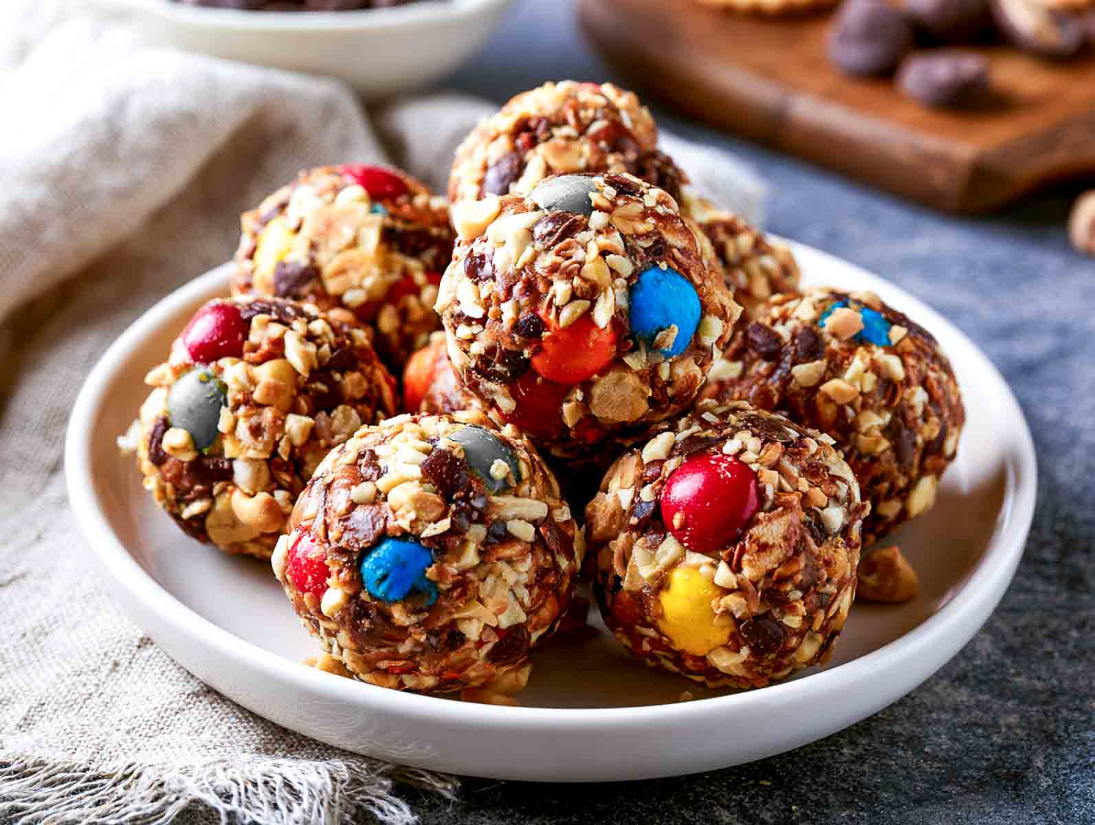 M&M monster high-protein energy balls packed with colorful candy-coated chocolates and chopped peanuts on a white plate.