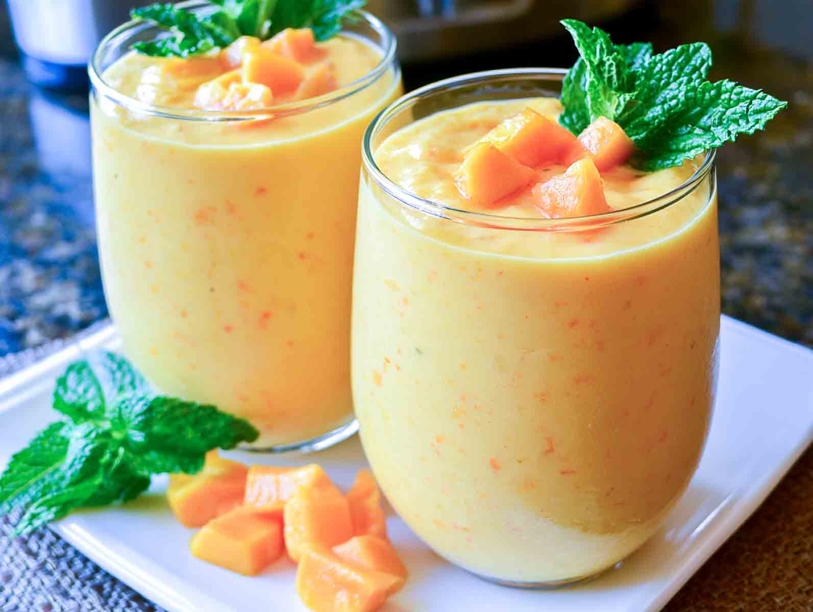Two glasses of mango kefir smoothie topped with diced mango and fresh mint.