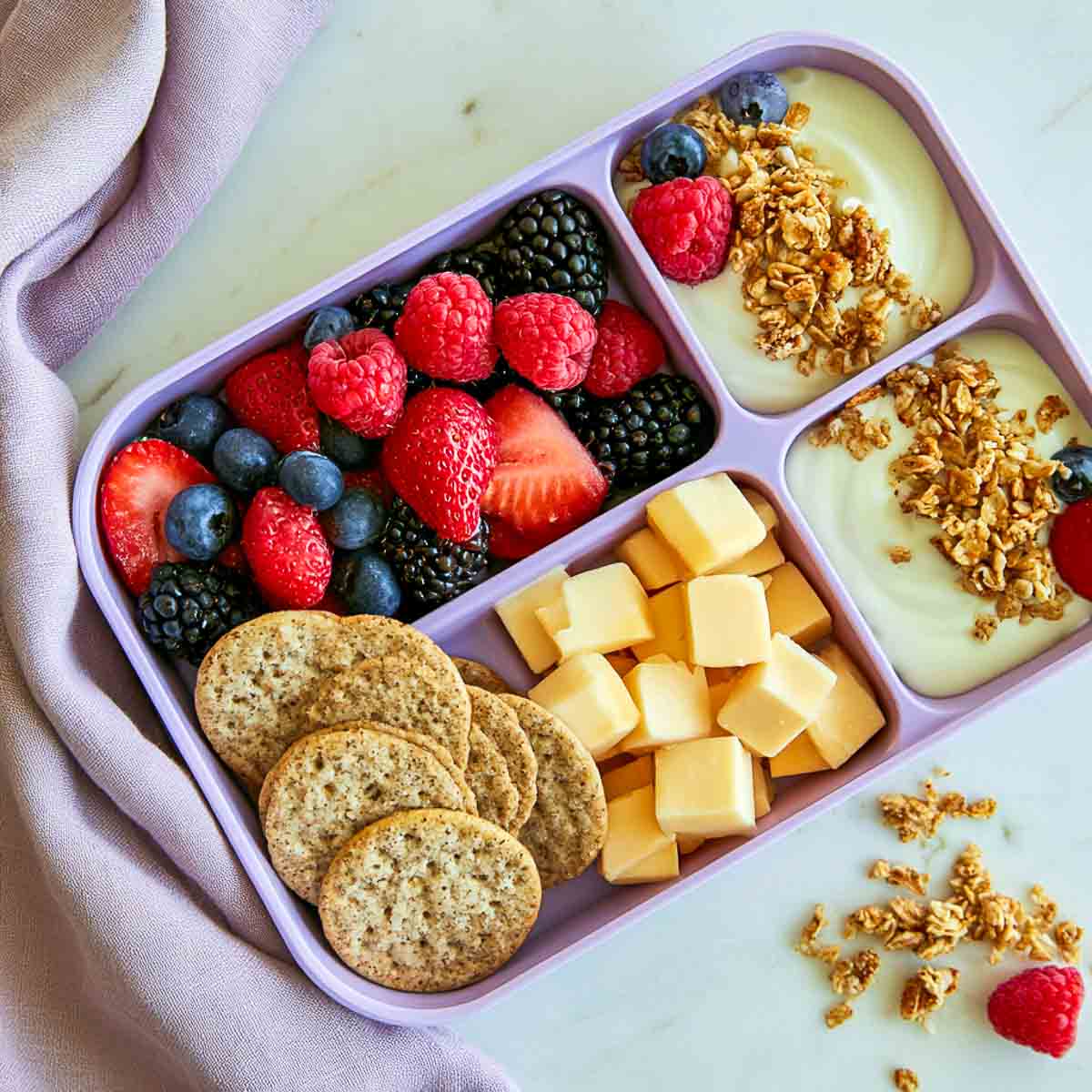 Mixed berry kefir parfait cups with granola, strawberries, blueberries, raspberries, and blackberries in a lunchbox.