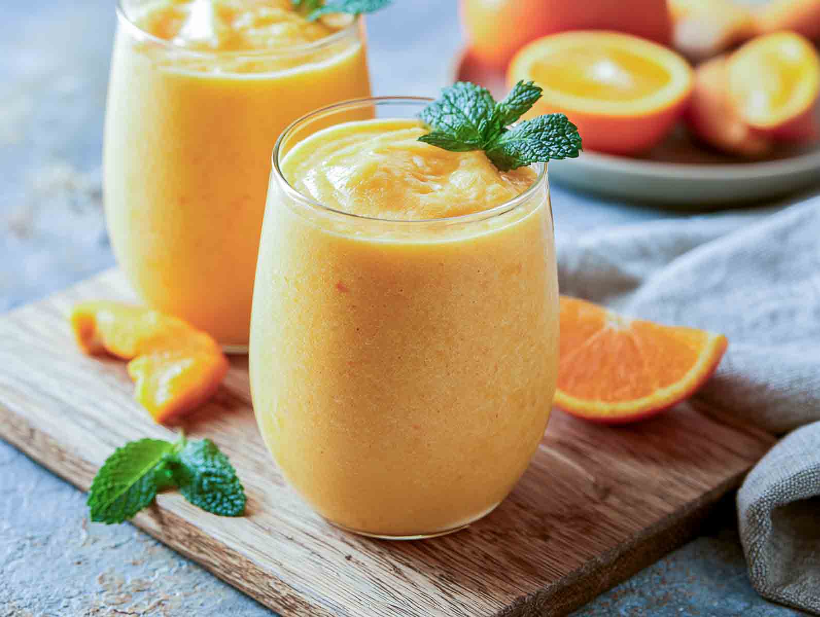 Orange kefir smoothie in a glass topped with fresh mint, with orange wedges alongside.