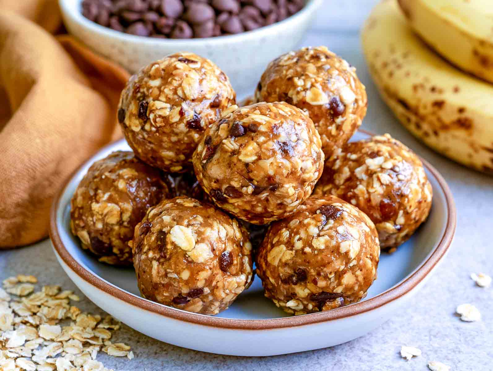 Protein powder banana oat high-protein energy balls with dried cranberries in a white bowl, with oats and dried cranberries behind.