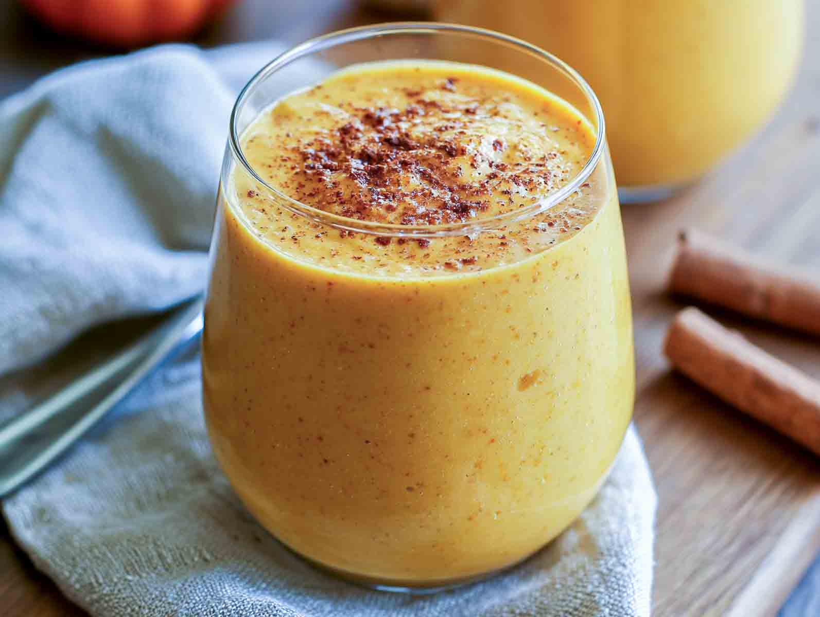 Pumpkin kefir smoothie in a glass dusted with pumpkin pie spice, with cinnamon sticks alongside.