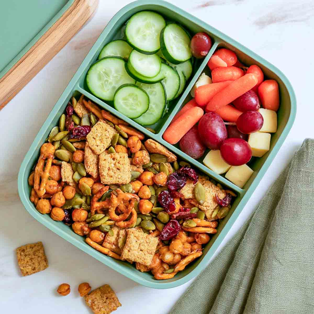 Nut-free pumpkin seed snack mix with roasted chickpeas, cereal, pretzels, crackers, and dried cranberries in a lunchbox.