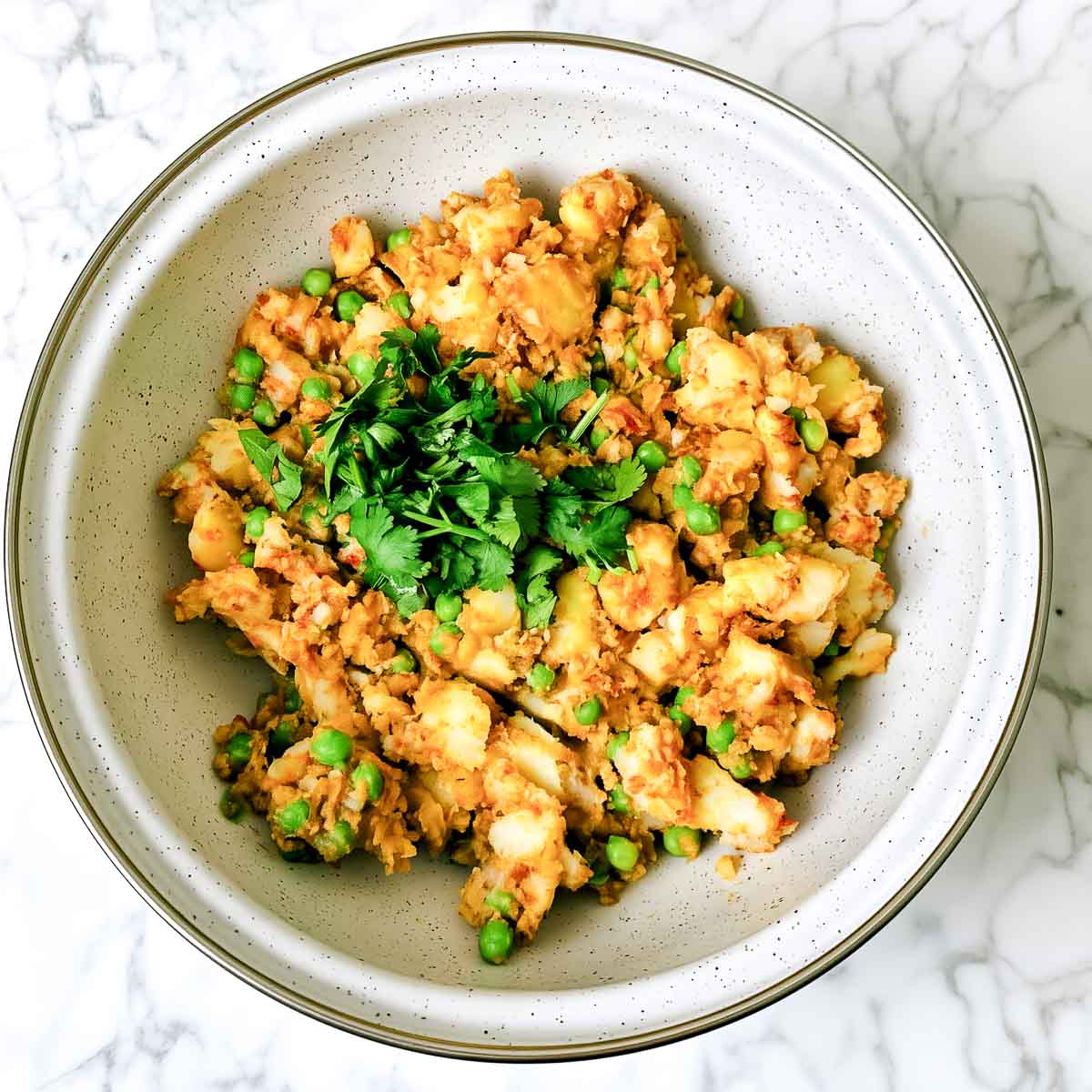 Spiced potato and pea samosa filling topped with fresh cilantro in a speckled white bowl.