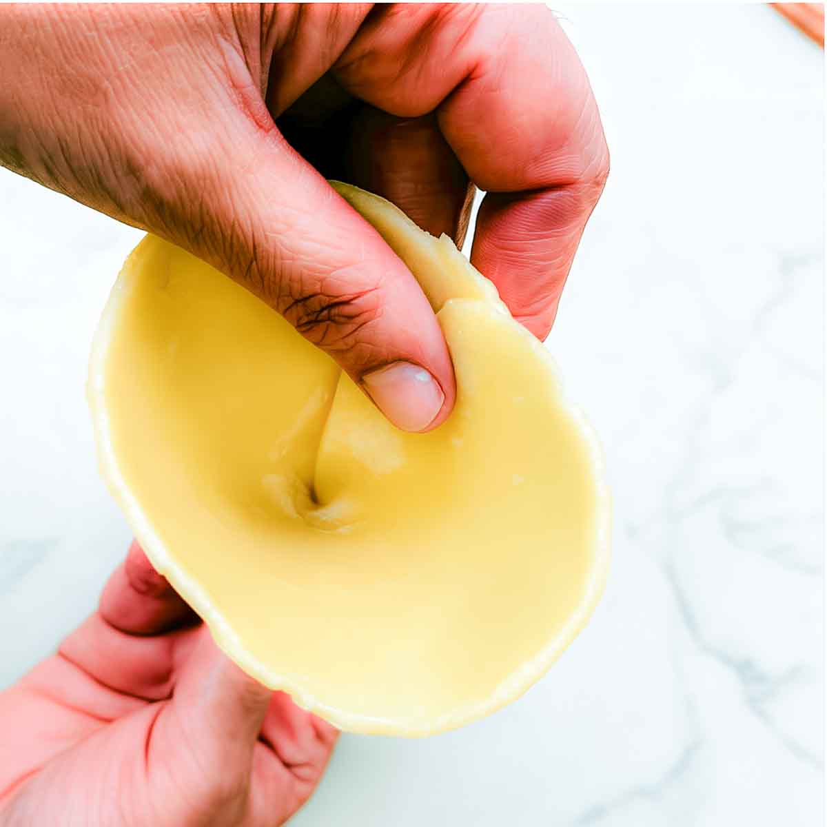 Hands hold a rolled piece of samosa dough that has been folded into a cone, ready to be filled.