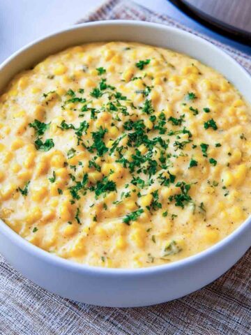 Creamy slow cooker creamed corn garnished with fresh parsley in a white bowl.