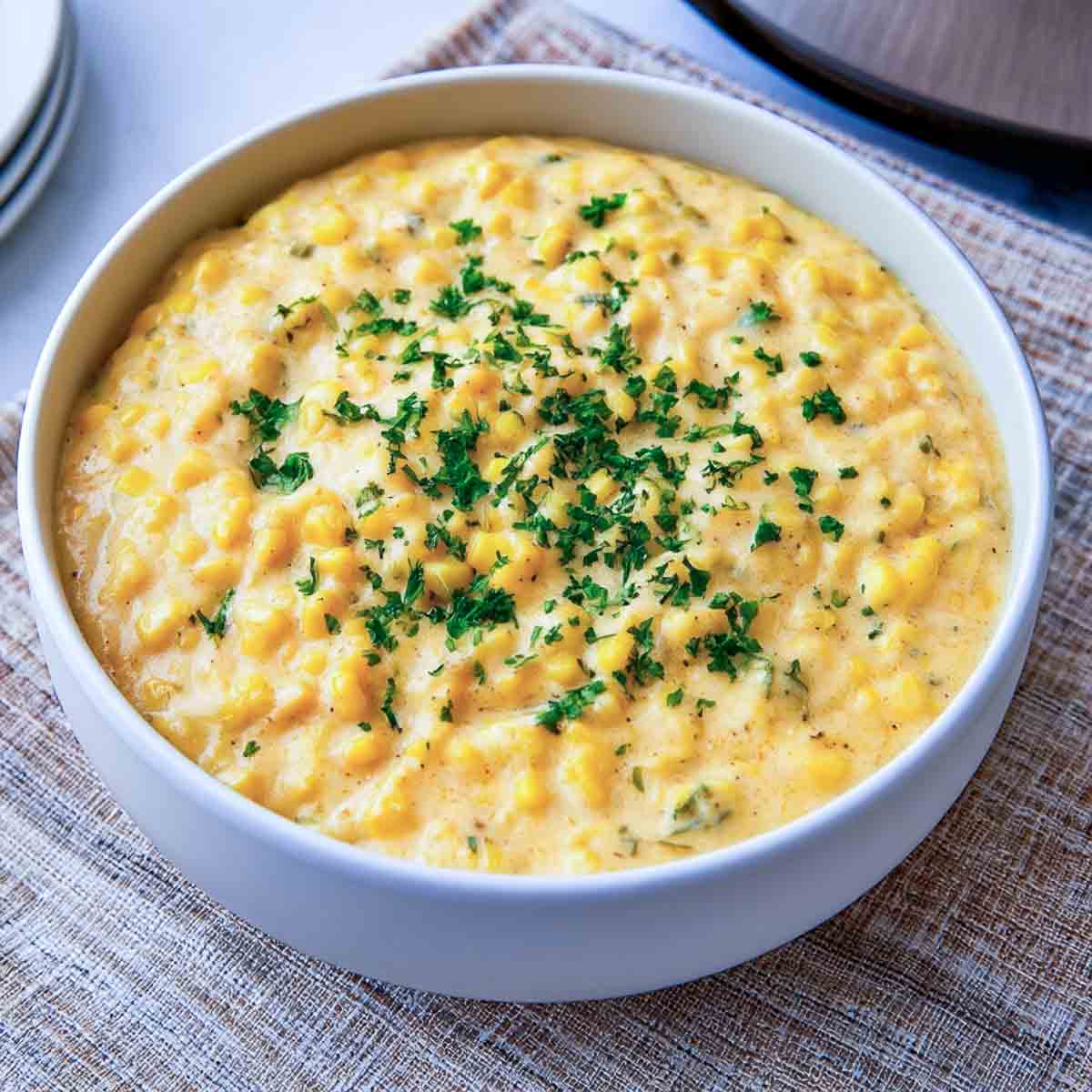 Creamy slow cooker creamed corn garnished with fresh parsley in a white bowl.