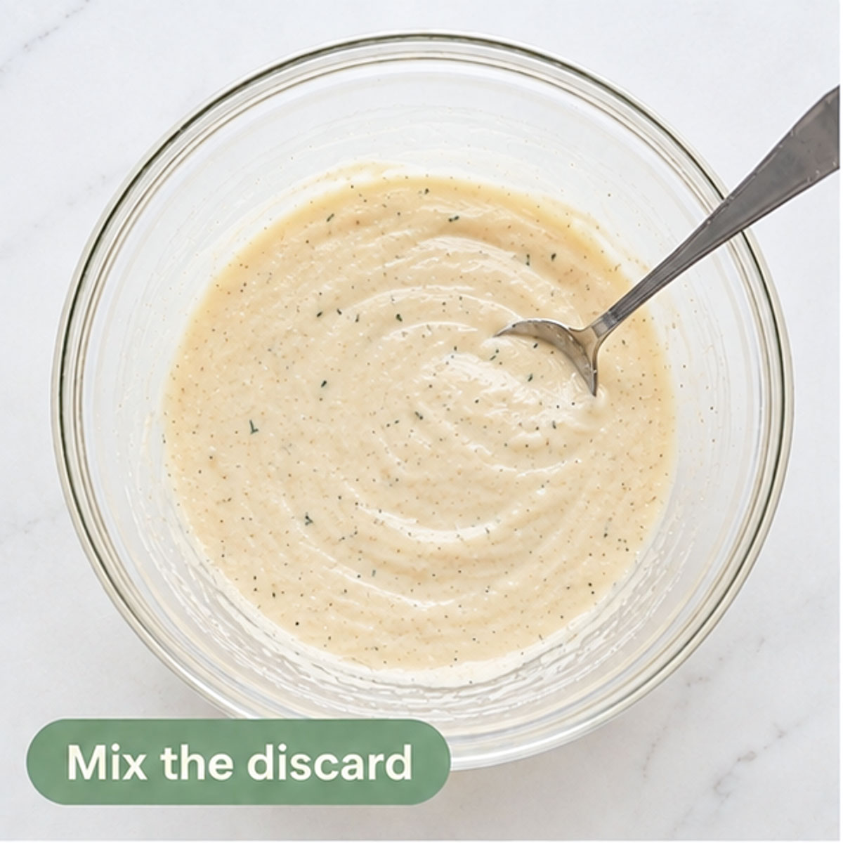 Sourdough discard mixture stirred with herbs in a glass bowl.