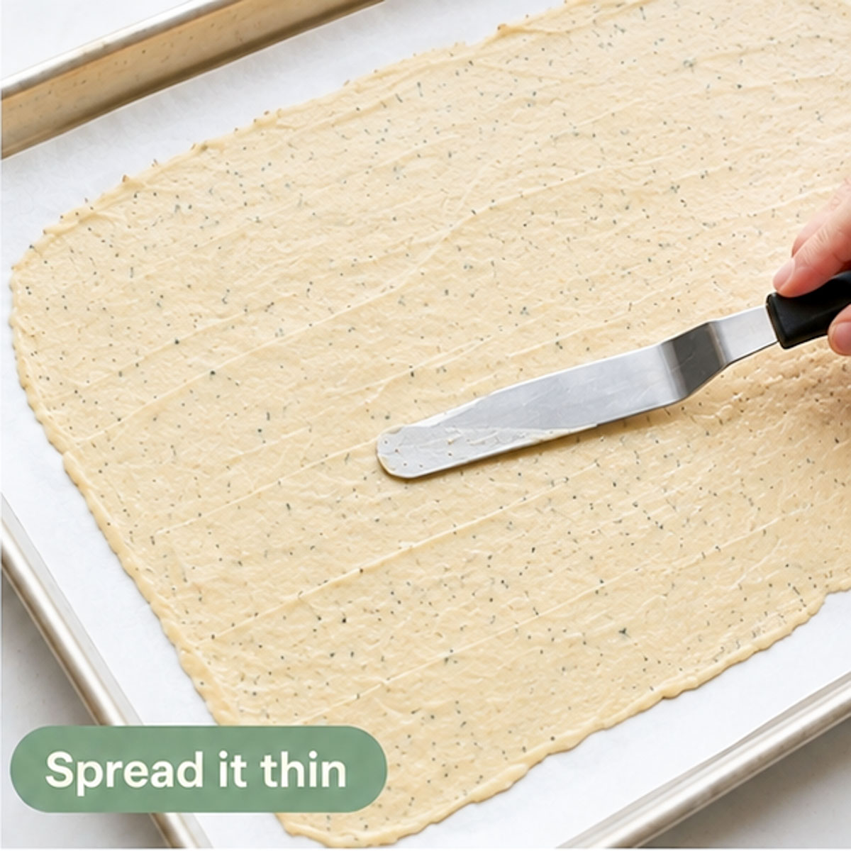 Sourdough cracker dough spread thinly over parchment paper on a baking sheet.