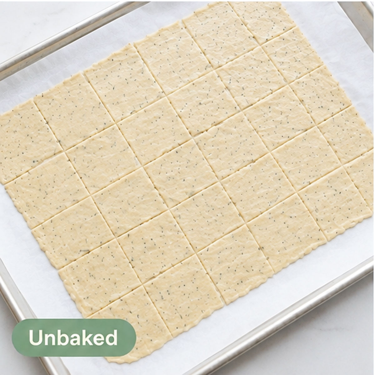 Thin sourdough cracker dough cut into square pieces on a parchment-lined baking sheet before baking.