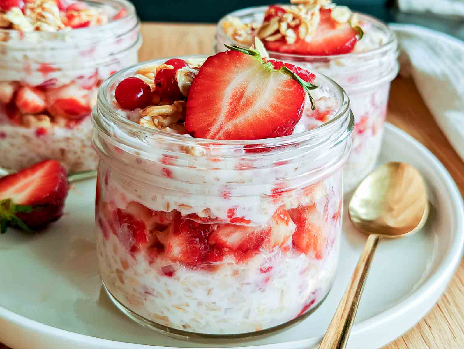 Strawberry kefir overnight oats layered with diced strawberries and topped with granola, a fresh strawberry, and red currants.