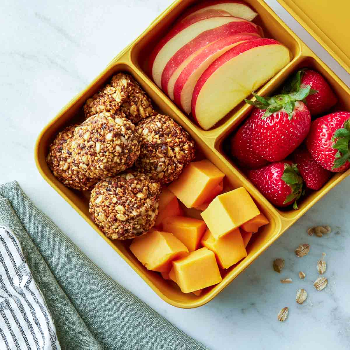 Sunflower seed energy bites with apple slices, strawberries, and cheese cubes packed in a lunchbox.