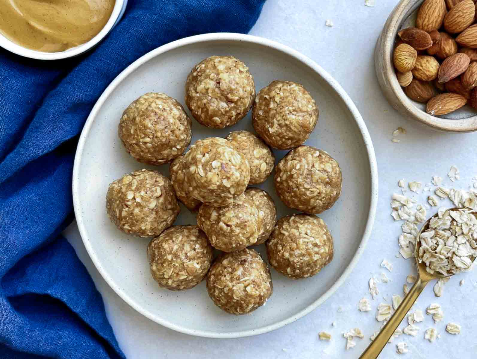 Toddler-friendly oatmeal high-protein energy balls on a white plate, with a spoonful of rolled oats, almonds, and nut butter alongside.