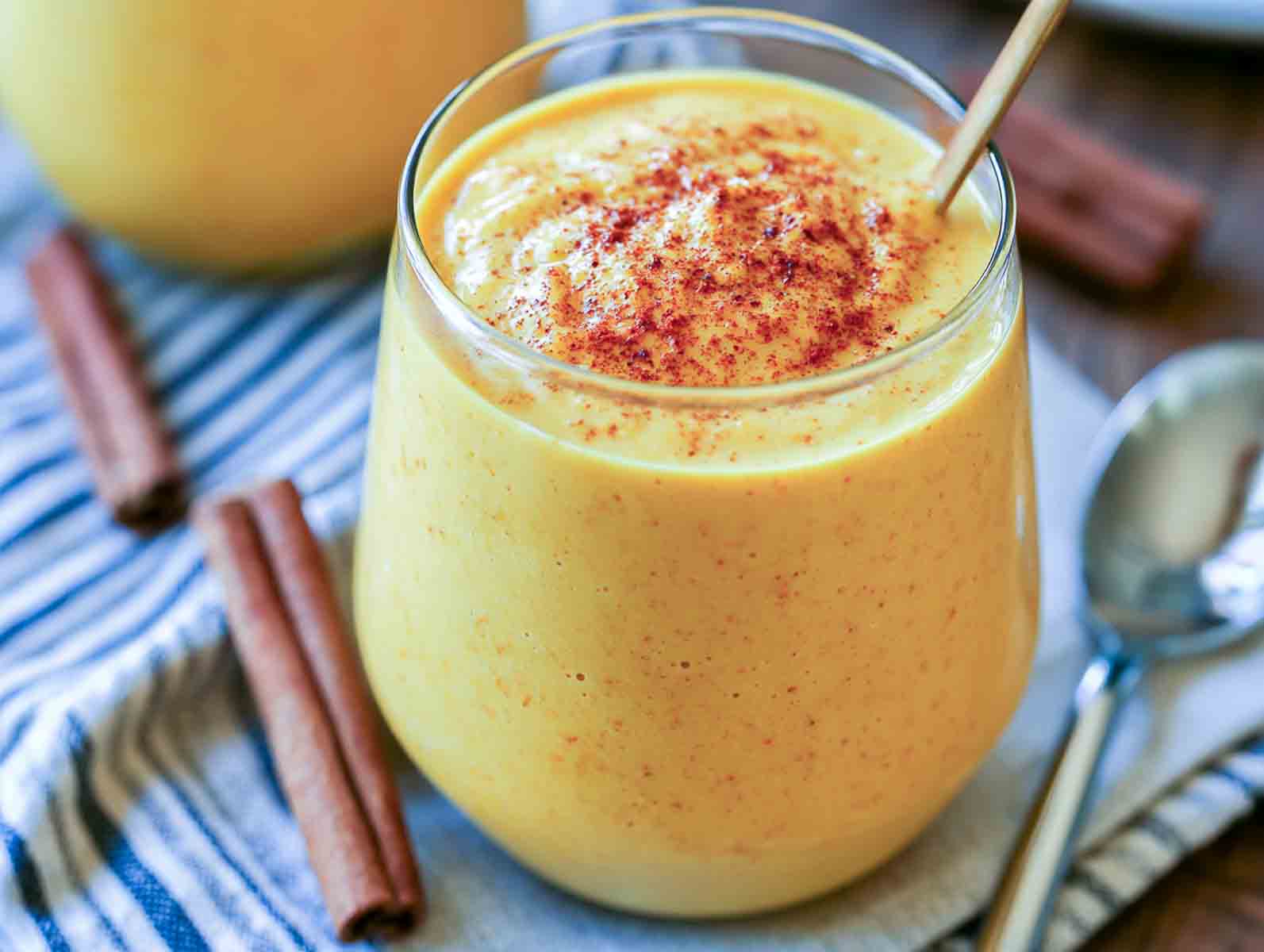 Golden turmeric kefir smoothie in a glass dusted with cinnamon, with cinnamon sticks alongside.